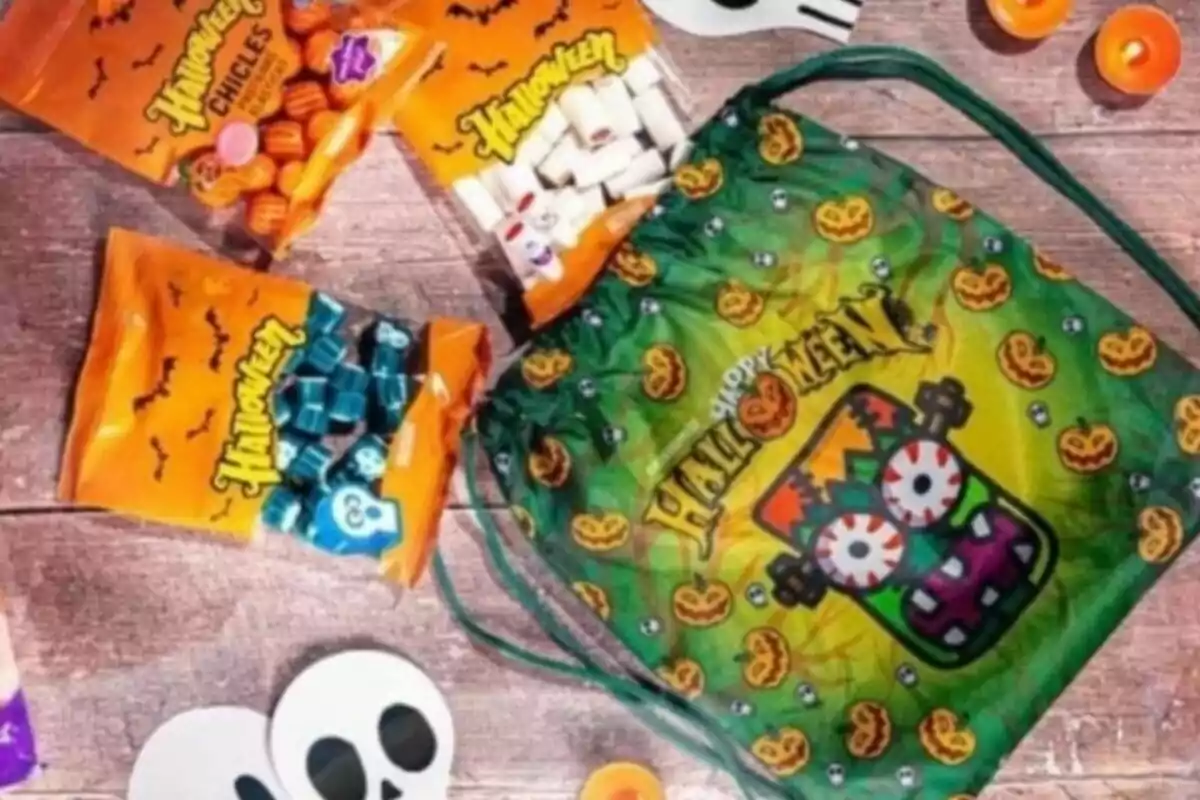 Una bolsa verde con diseño de Halloween y varios paquetes de dulces temáticos sobre una mesa de madera. Una bolsa verde con diseño de Halloween y varios paquetes de dulces temáticos sobre una mesa de madera.