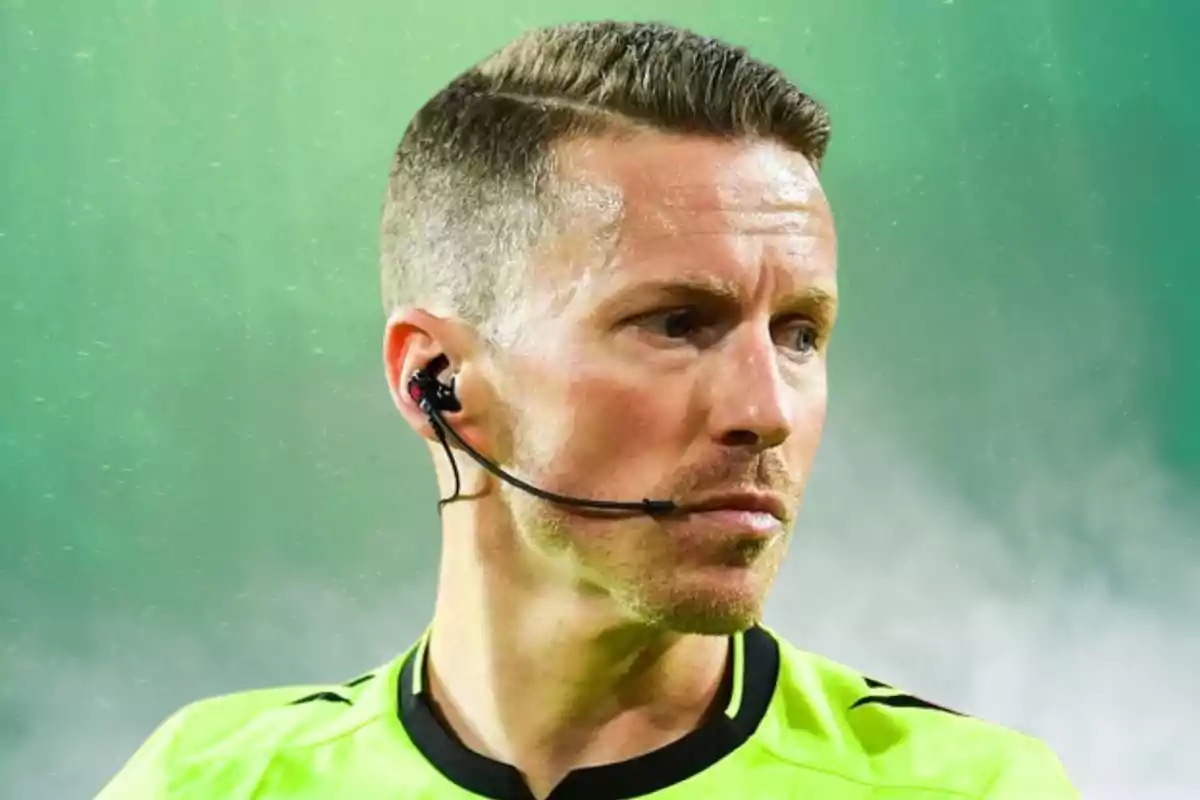 Un árbitro de fútbol con uniforme verde y auricular en un ambiente deportivo.
