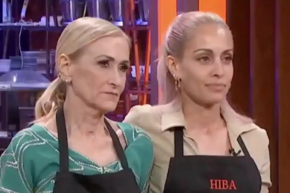 Cristina Cifuentes y Hiba Abouk con delantales negros están de pie en un entorno de cocina en MasterChef Celebrity.