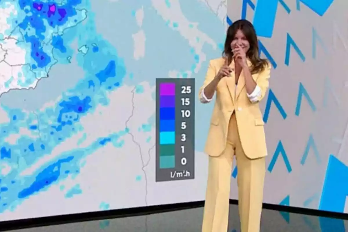 Himar González en Antena 3 Noticias, vestida con un traje amarillo, señala y sonríe mientras muestra un mapa meteorológico con diferentes niveles de precipitación.