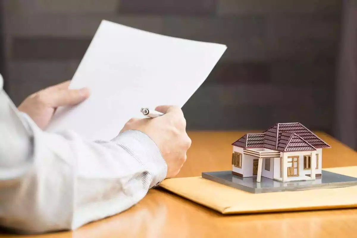 Una persona con un papel y un boli y una maqueta de una casa en miniatura encima de una mesa