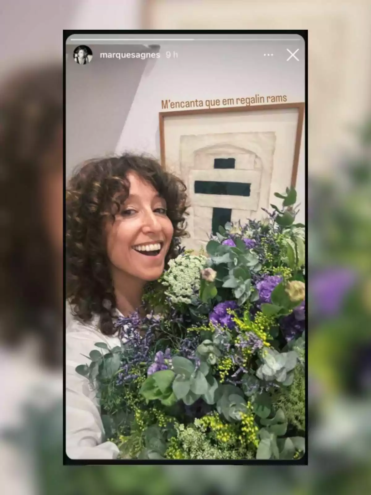 Una persona sonriente sostiene un ramo de flores coloridas frente a una obra de arte en la pared. Una persona sonriente sostiene un ramo de flores coloridas frente a una obra de arte en la pared.
