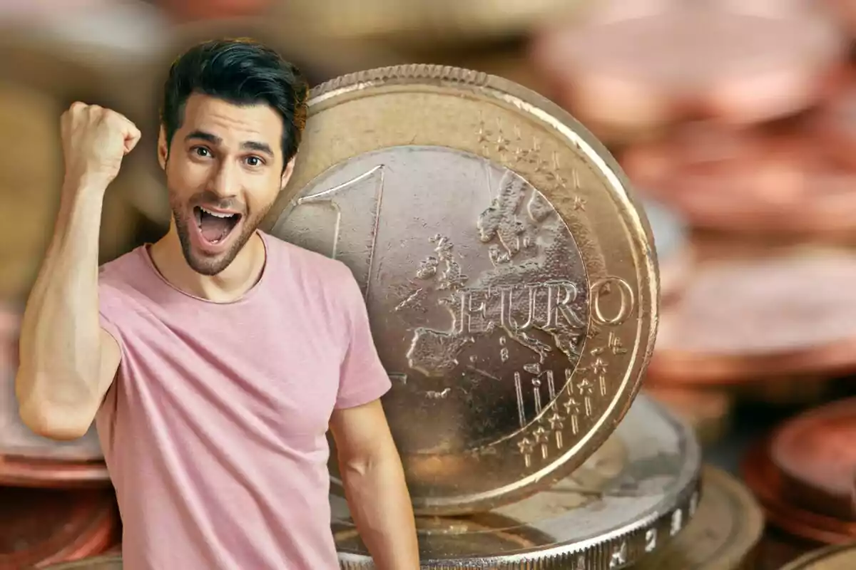 Un hombre joven con camiseta rosa celebra con el puño levantado frente a una gran moneda de un euro.