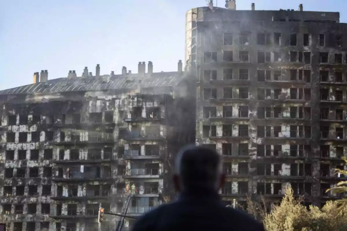 Un hombre en primer plano observando el edificio de viviendas quemado en Valencia