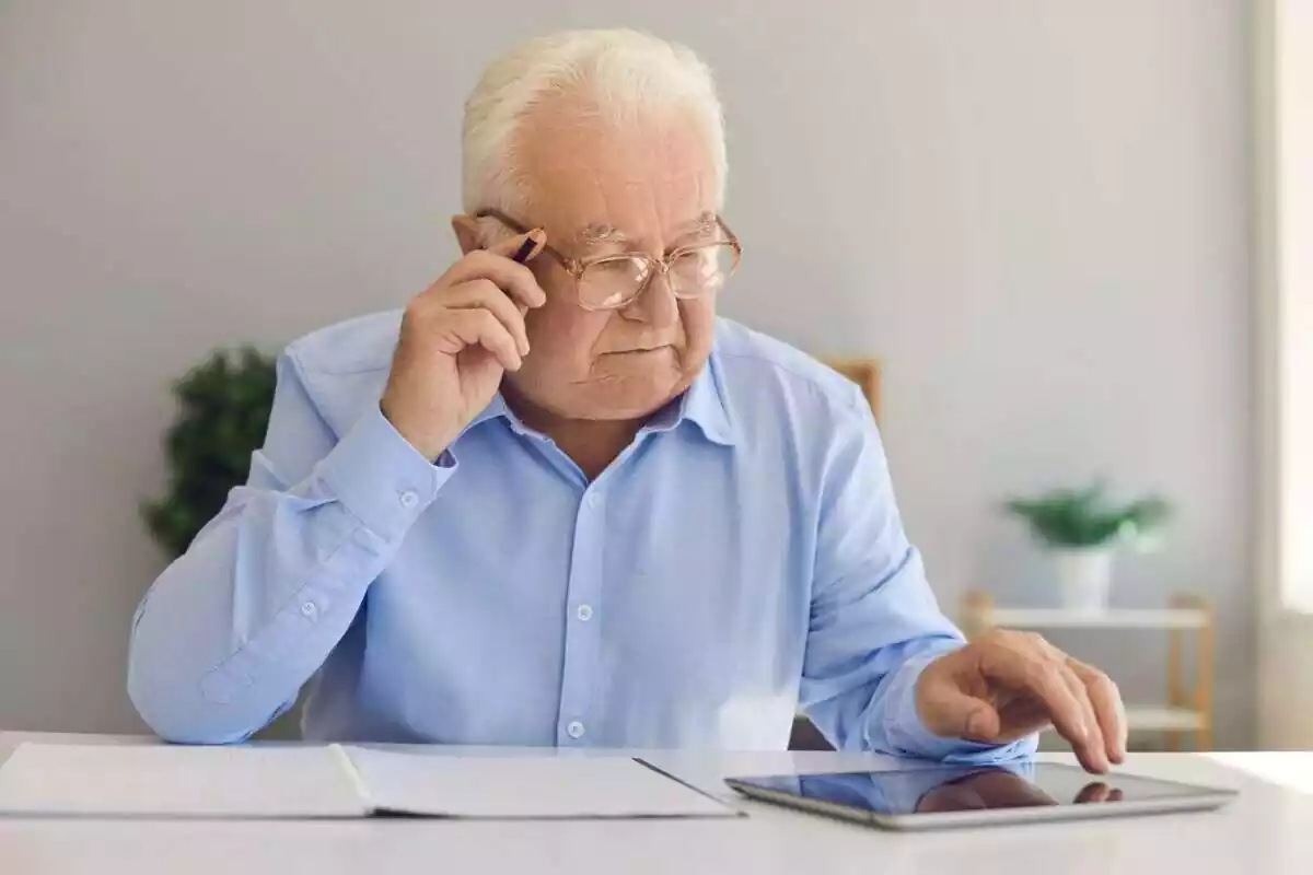 Un hombre mayor haciendo papeleo con una tablet, una libreta y un lápiz
