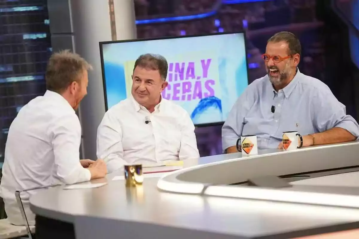 Martín Berasategui y David de Jorge junto a Pablo Motos conversan y ríen en El Hormiguero con una pantalla de fondo que muestra texto en colores brillantes.