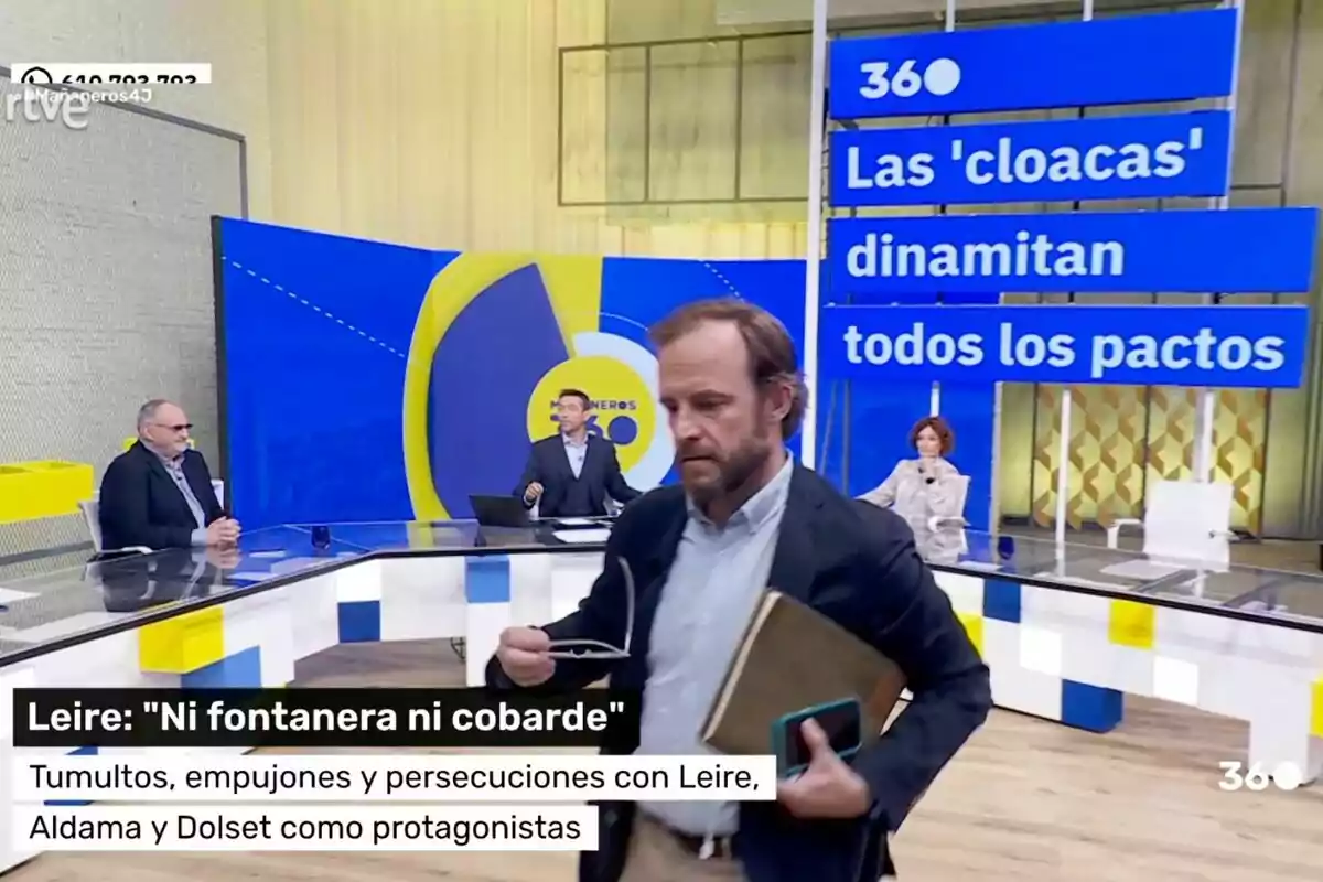 Chapu Apaolaza abandona con una carpeta y un móvil en la mano 'Mañaneros' con varias personas sentadas en una mesa y un gran letrero azul que dice Las 'cloacas' dinamitan todos los pactos