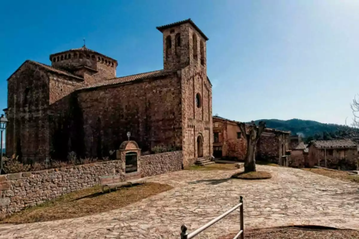 Iglesia de piedra antigua con un camino empedrado y un árbol sin hojas en un entorno rural. Iglesia de piedra antigua con un camino empedrado y un árbol sin hojas en un entorno rural.