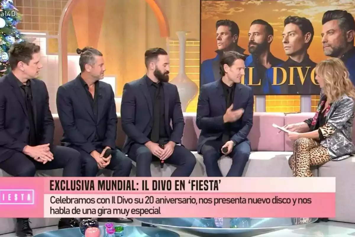 Un grupo de hombres vestidos de traje oscuro está sentado en un set de Fiesta junto a Emma García, con un cartel de fondo que dice 