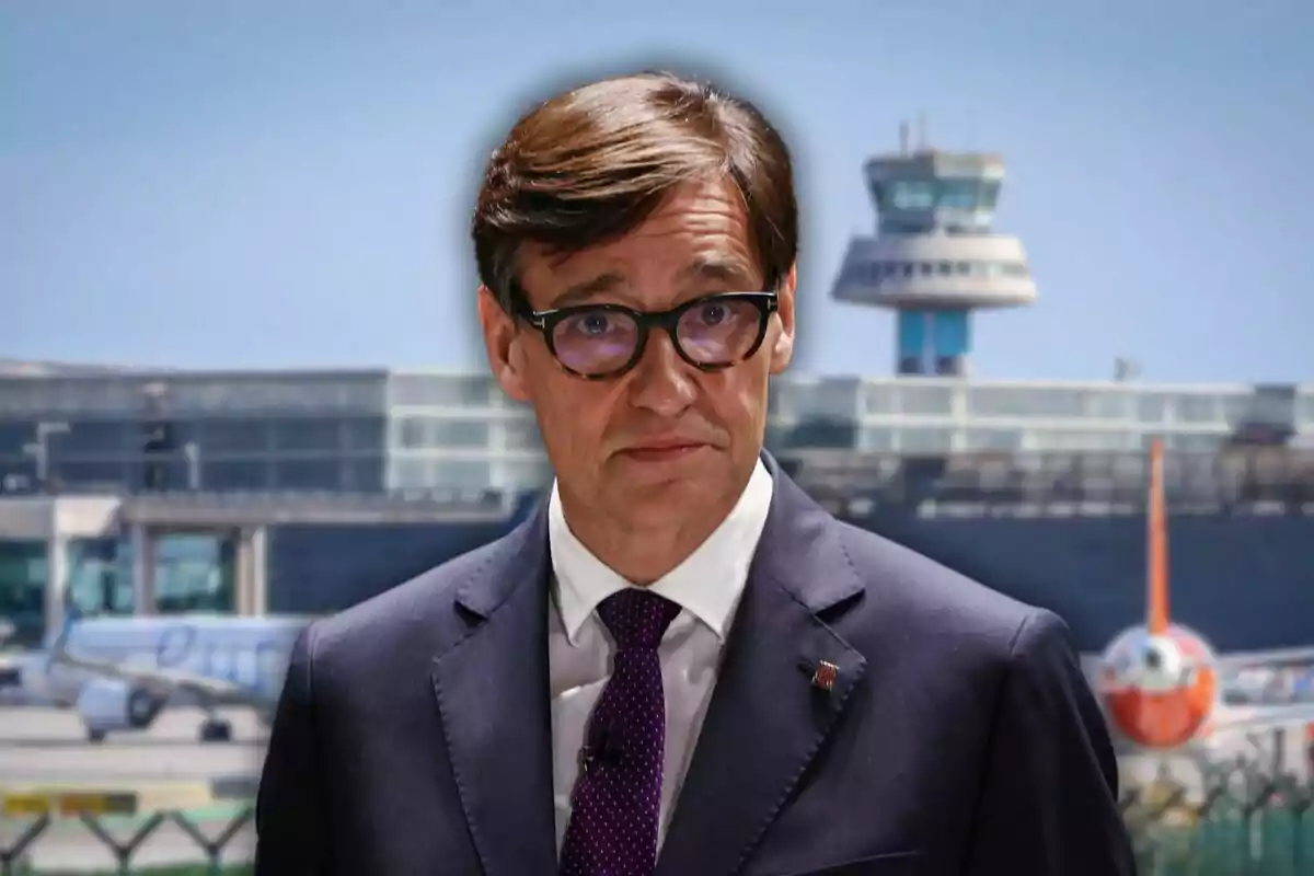 Hombre con gafas y traje oscuro de pie frente a un aeropuerto con aviones y torre de control al fondo
