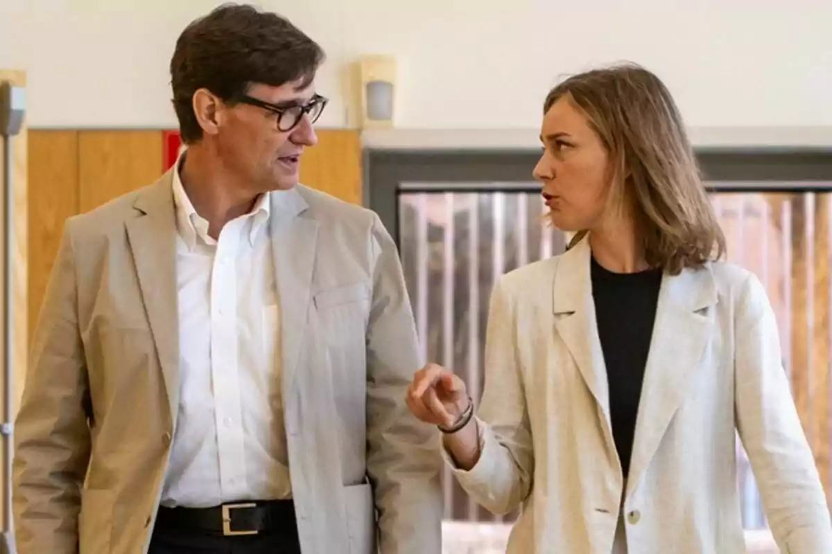 Dos personas conversando mientras caminan en un interior con paredes de madera.
