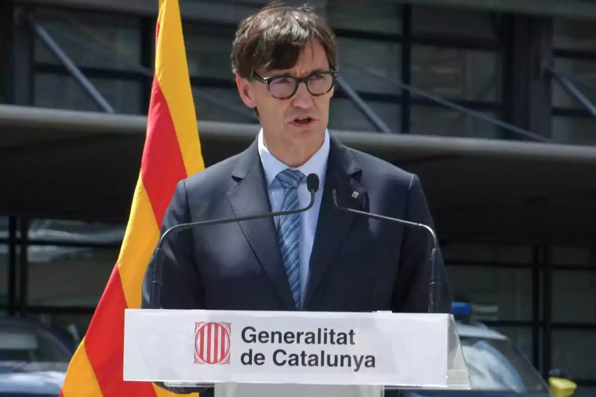 Salvador Illa en un podio con el logo de la Generalitat de Catalunya y una bandera catalana de fondo.