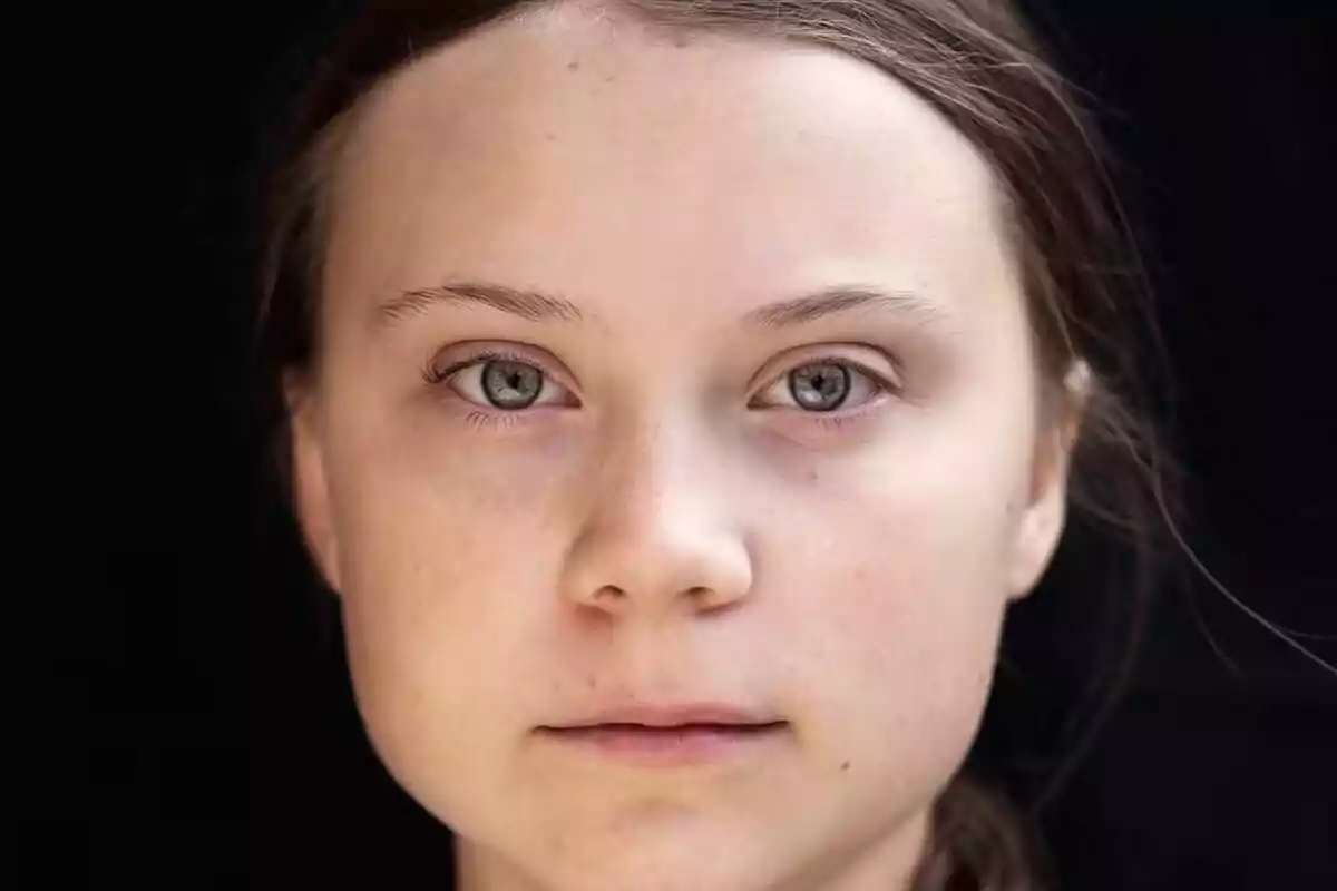 Primer plano de una joven de cabello castaño y ojos claros con expresión seria sobre fondo negro
