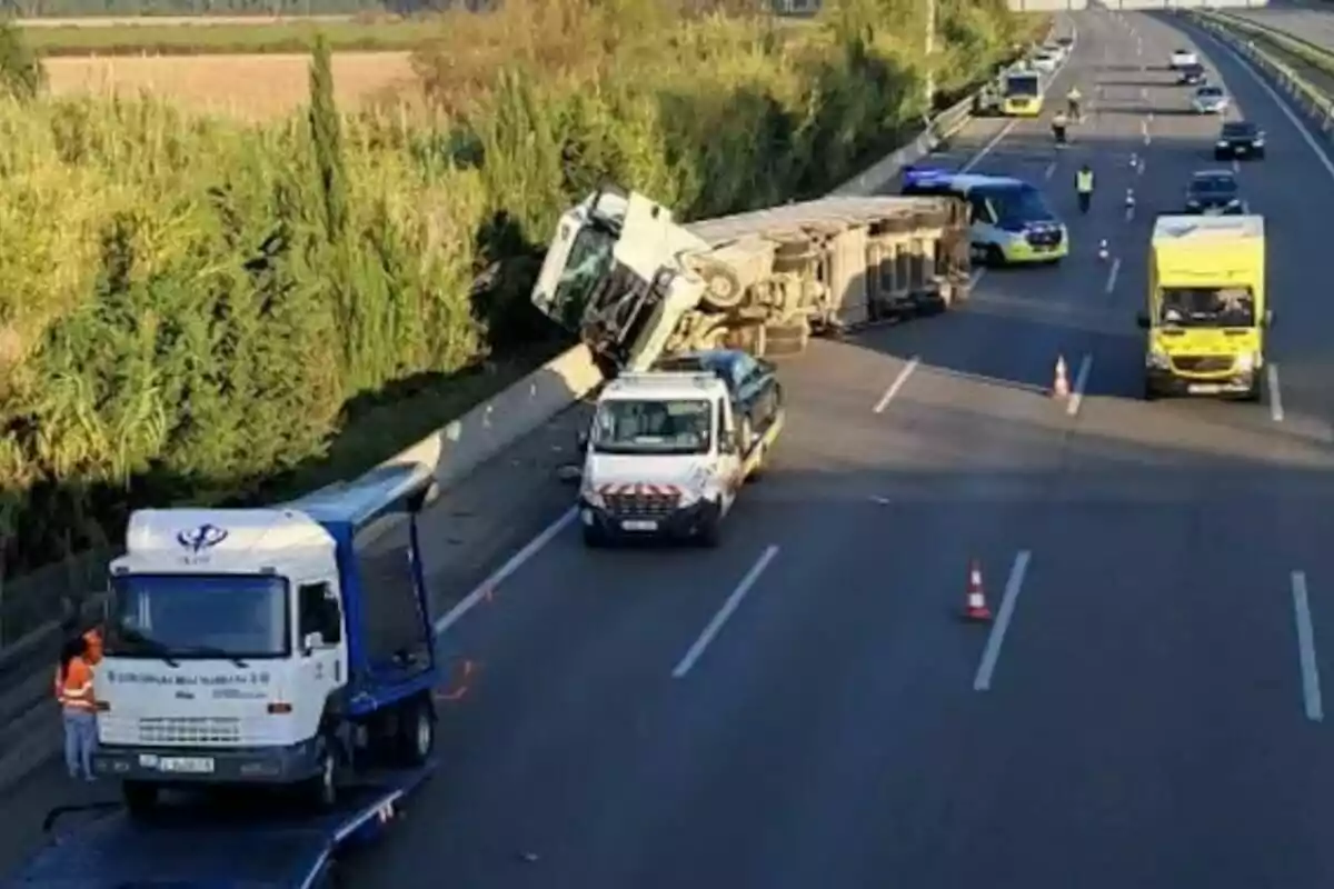 Un camión volcado en una autopista con varios vehículos de asistencia y señalización de tráfico presentes.