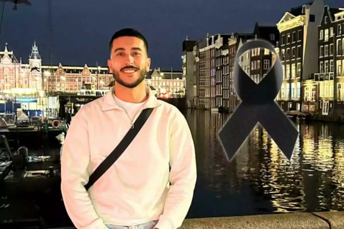 Un hombre sonriente con barba y suéter claro posa frente a un canal iluminado por la noche con un lazo negro superpuesto en la imagen.