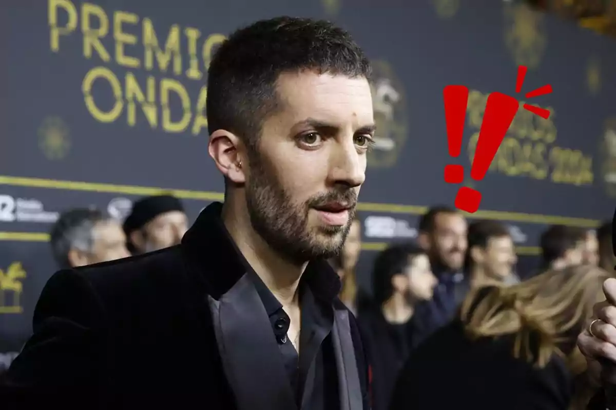 David Broncano con barba y cabello corto en un evento de los Premios Ondas, con un fondo de personas y un símbolo de exclamación rojo al lado.