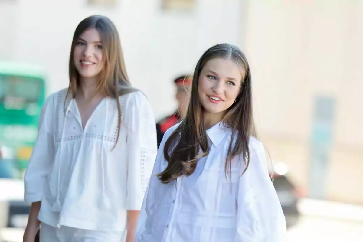 Dos jóvenes sonrientes con camisas blancas posan al aire libre.