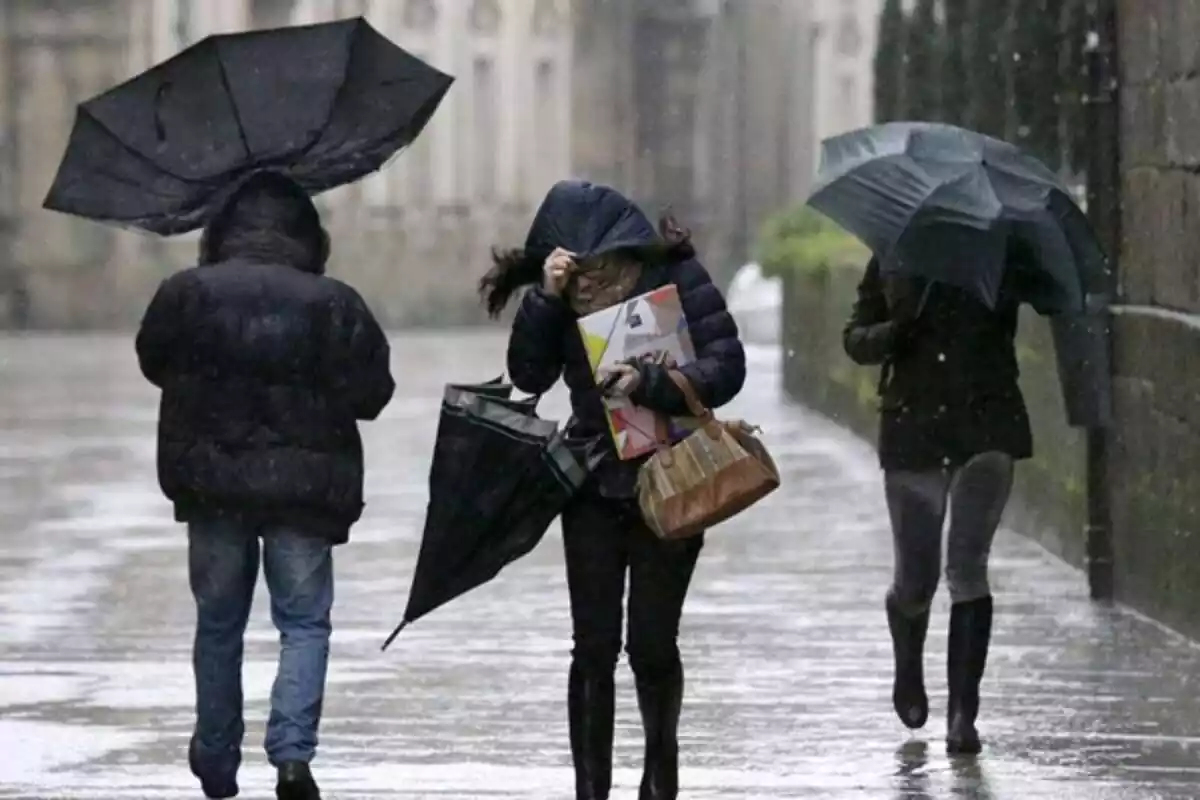 Personas con paraguas andando por la calle mientras hace un temporal de lluvia y viento