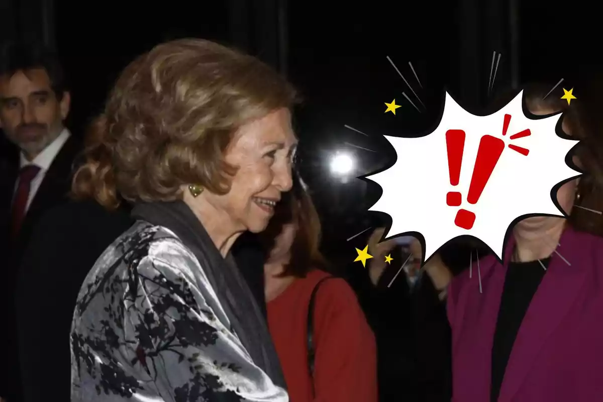 La reina Sofía sonríe mientras saluda a otra persona cuya cara está cubierta por un gráfico de exclamación en un evento formal.