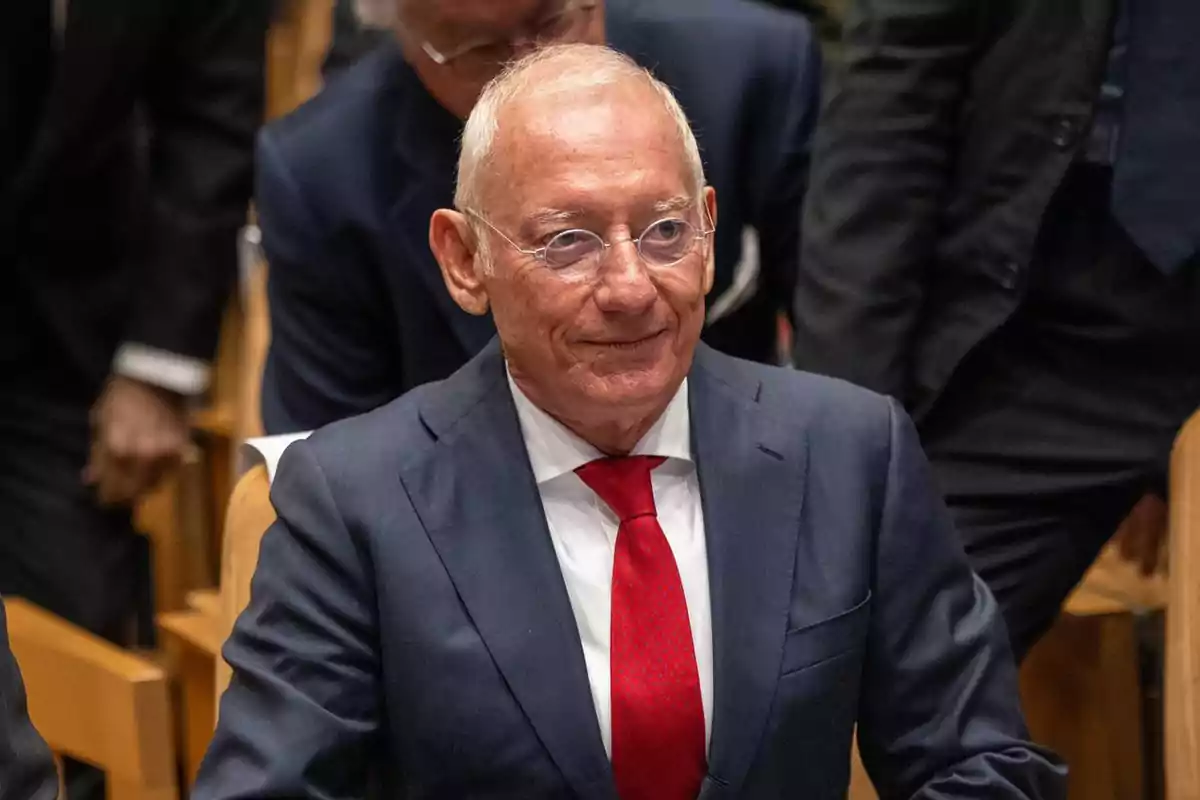 Isak Andic con gafas y traje oscuro con corbata roja sentado en un evento formal.