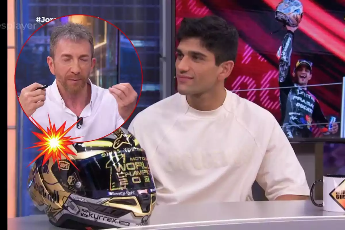 Jorge Martín y Pablo Motos en un programa de televisión, uno de ellos sostiene un casco de motocicleta con la inscripción "World Champion 2023" mientras el otro parece estar hablando, en el fondo se ve una imagen de un piloto celebrando.