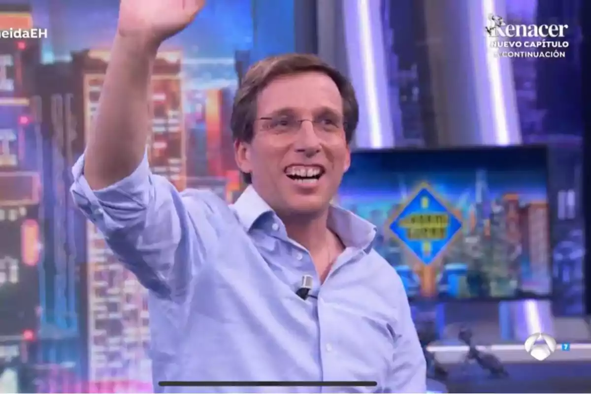 José Luis Martínez-Almeida con camisa azul sonríe y saluda en un set de televisión colorido.