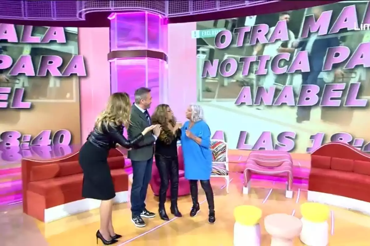 Un grupo de personas interactúa en un colorido set de televisión con un gran cartel de fondo que muestra un mensaje. Un grupo de personas interactúa en un colorido set de televisión con un gran cartel de fondo que muestra un mensaje.