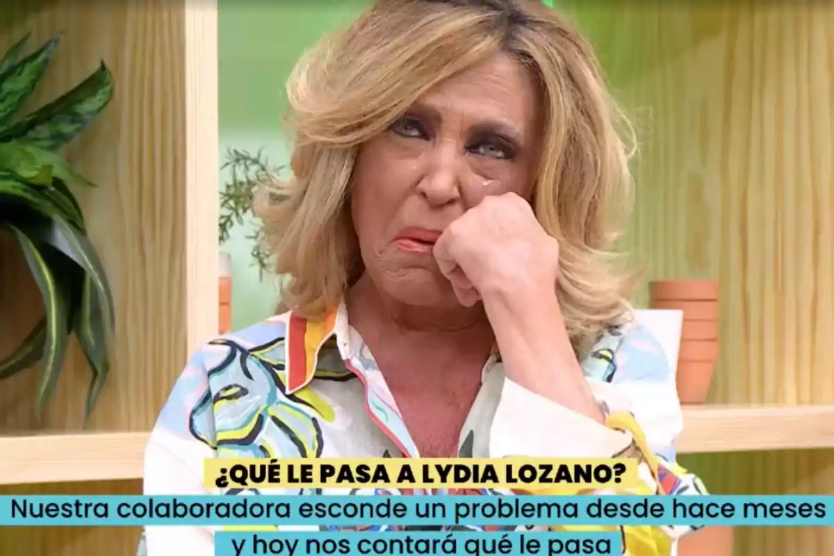Lydia Lozano rubia con expresión triste y lágrimas en los ojos, sentada en un set de televisión con plantas de fondo y un texto en pantalla que pregunta qué le pasa a Lydia Lozano Lydia Lozano rubia con expresión triste y lágrimas en los ojos, sentada en un set de televisión con plantas de fondo y un texto en pantalla que pregunta qué le pasa a Lydia Lozano