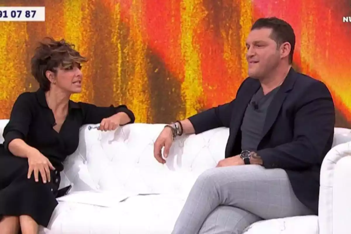 Sonsoles Ónega y Manu Tenorio sentados en un sofá blanco conversando en un set de televisión con un fondo de colores cálidos. Sonsoles Ónega y Manu Tenorio sentados en un sofá blanco conversando en un set de televisión con un fondo de colores cálidos.