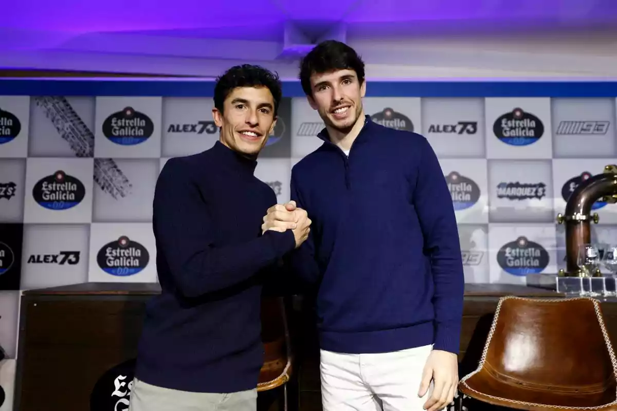 Dos personas posan juntas estrechando sus manos en un evento con un fondo de logotipos de Estrella Galicia. Dos personas posan juntas estrechando sus manos en un evento con un fondo de logotipos de Estrella Galicia.