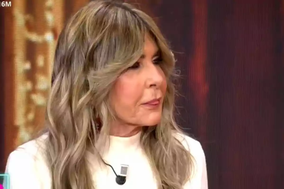 Marisa Martín-Blázquez con cabello largo y rubio ceniza, vestida con una blusa blanca, está participando en un programa de televisión.