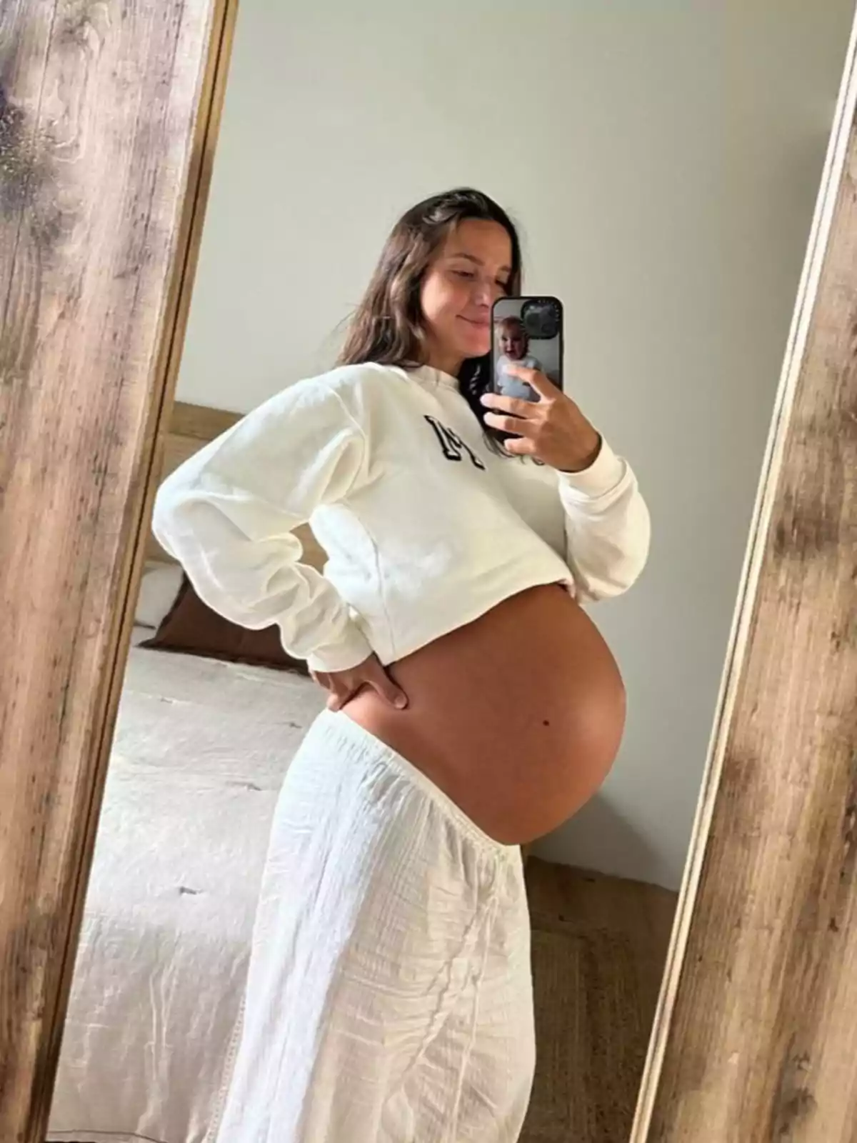 Marta Pombo embarazada tomándose una selfie frente a un espejo, vistiendo una sudadera blanca y una falda larga blanca. Marta Pombo embarazada tomándose una selfie frente a un espejo, vistiendo una sudadera blanca y una falda larga blanca.