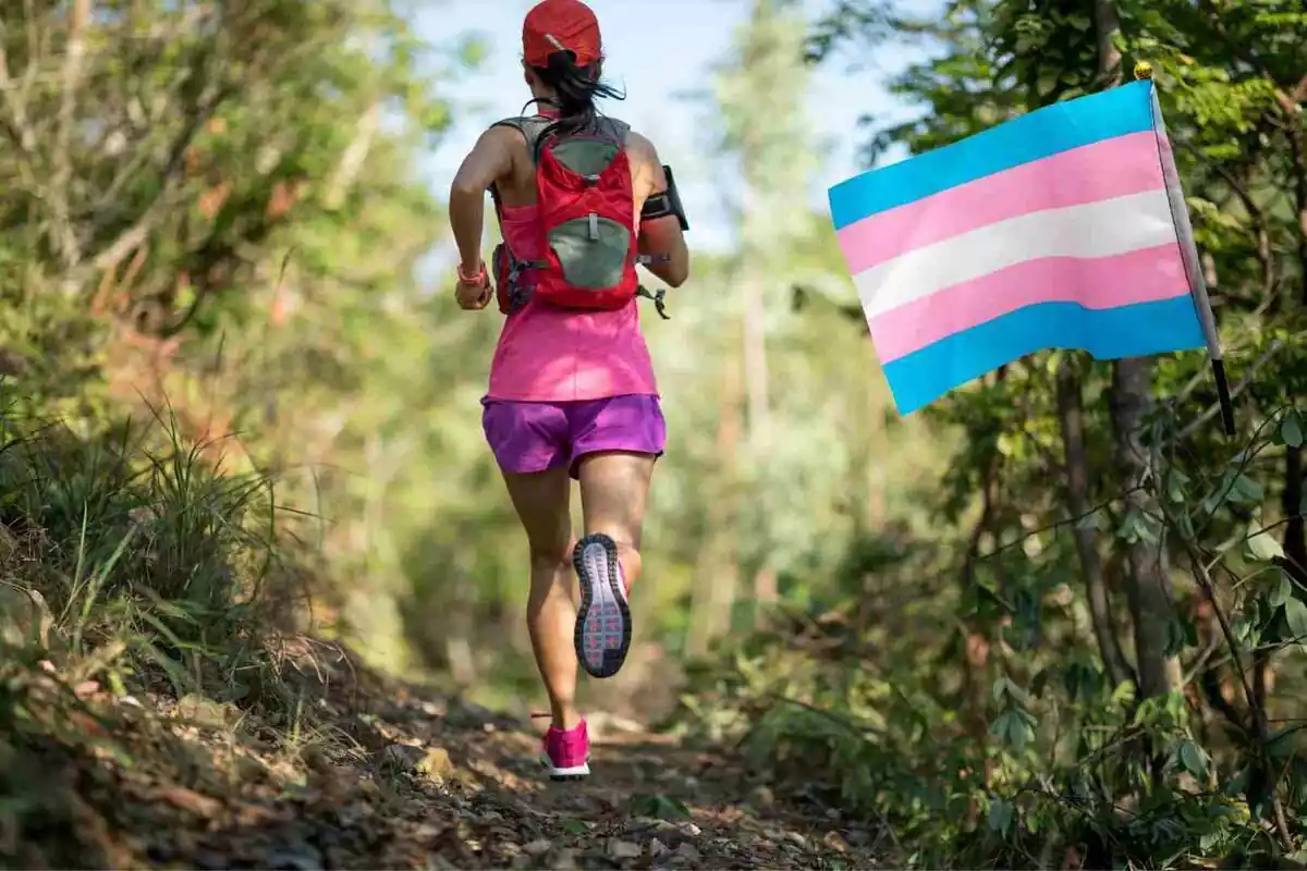 Mujer atleta corriendo de espaldas junto a una bandera del colectivo trans