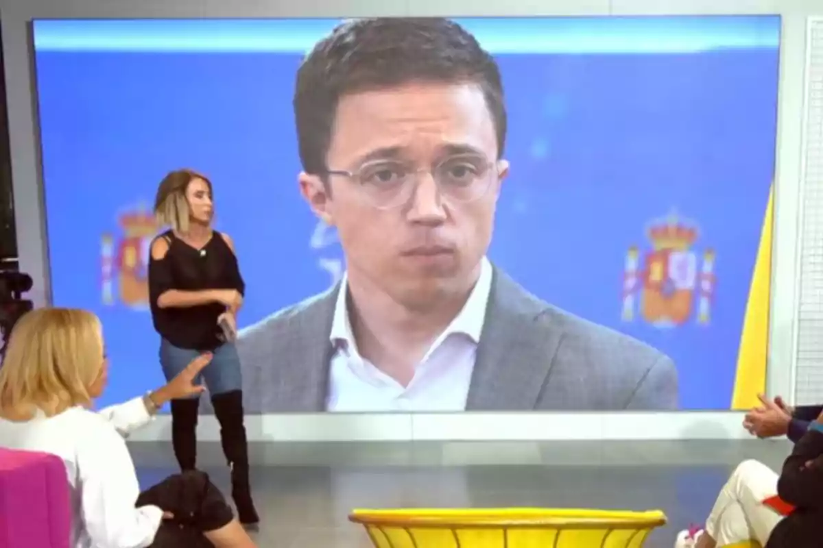 Un programa de televisión con un gran monitor que muestra a Íñigo Errejón con gafas y traje mientras varias personas conversan en el set.