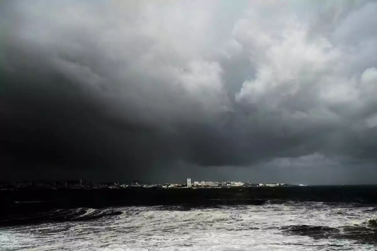 Cielo nublado y oscuro sobre un mar agitado con una ciudad en el horizonte. Cielo nublado y oscuro sobre un mar agitado con una ciudad en el horizonte.