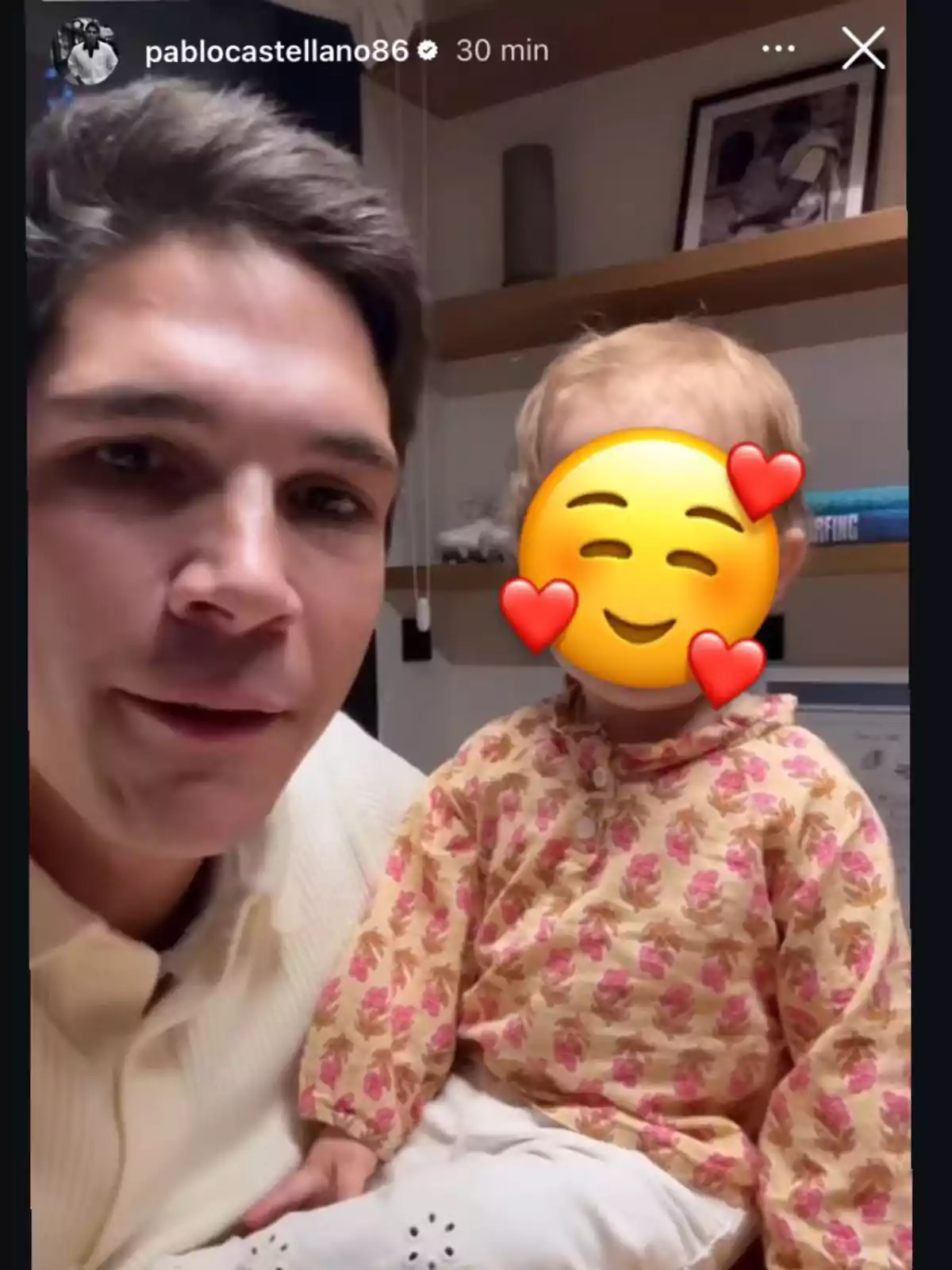 Pablo Castellano con un suéter claro sostiene a un niño pequeño cuyo rostro está cubierto por un emoji sonriente con corazones en las mejillas. Pablo Castellano con un suéter claro sostiene a un niño pequeño cuyo rostro está cubierto por un emoji sonriente con corazones en las mejillas.
