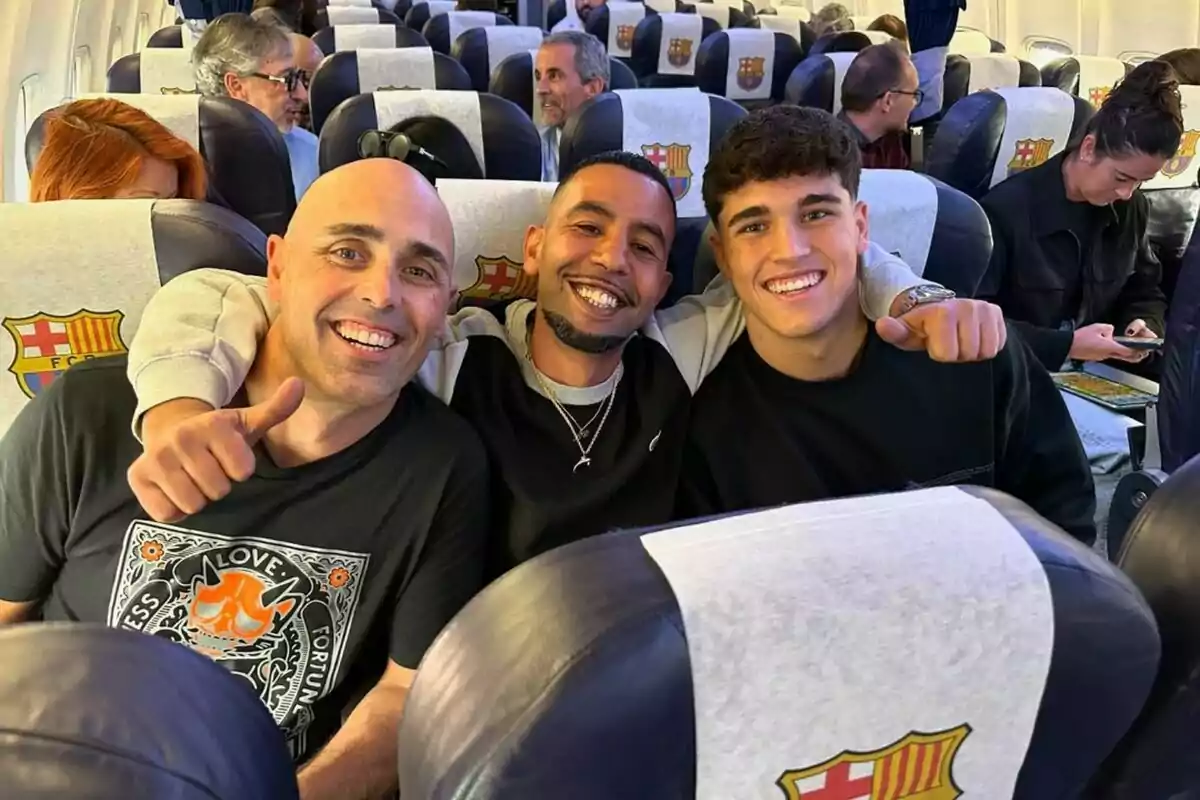 Tres personas sonrientes sentadas en un avión con asientos que tienen el escudo del FC Barcelona. Tres personas sonrientes sentadas en un avión con asientos que tienen el escudo del FC Barcelona.