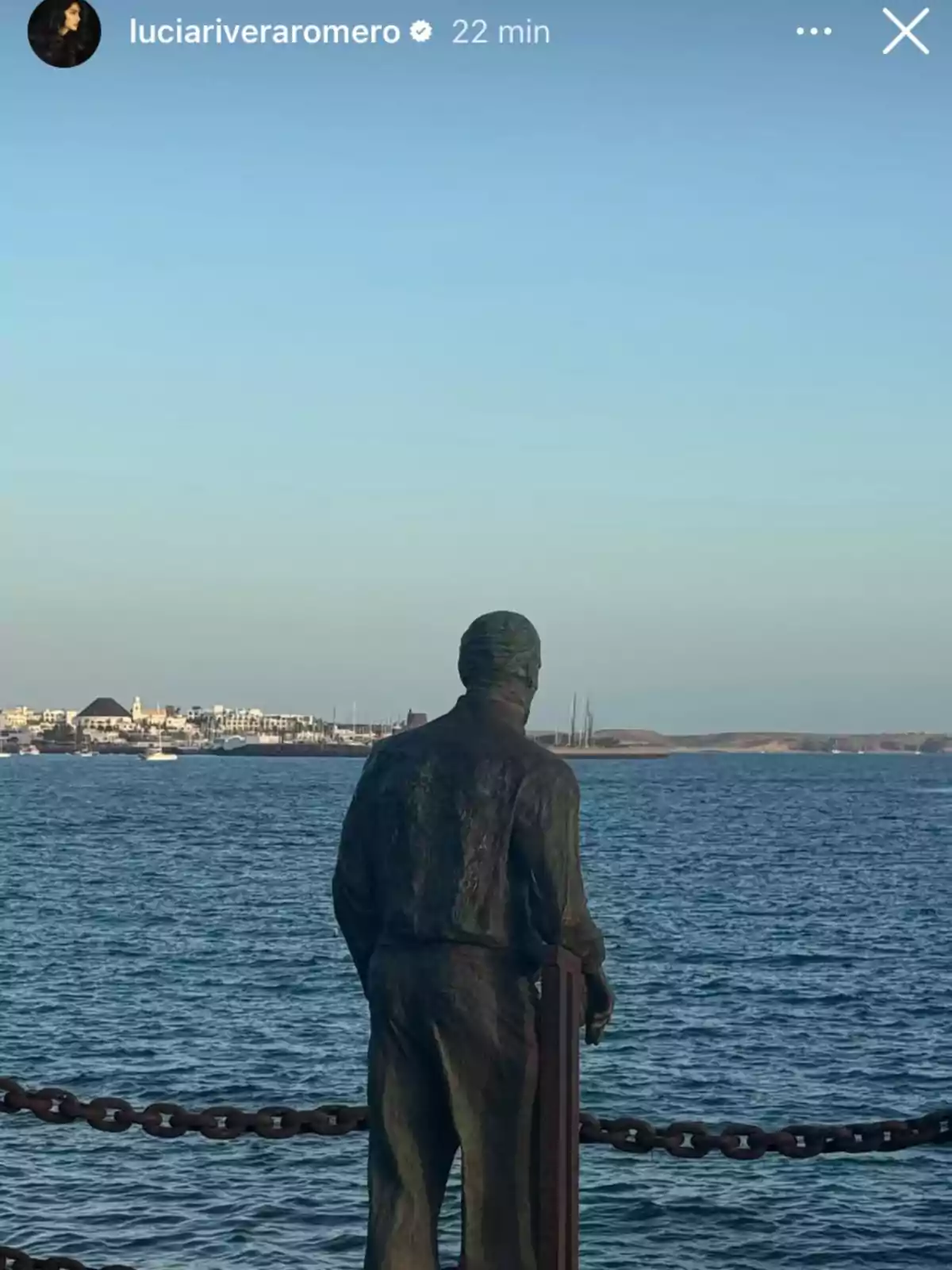 Una estatua de un hombre mirando hacia el mar con un pueblo costero al fondo. Una estatua de un hombre mirando hacia el mar con un pueblo costero al fondo.