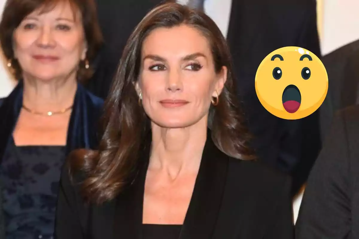 La reina Letizia con cabello castaño y expresión seria está en un evento formal con un emoji sorprendido al lado.