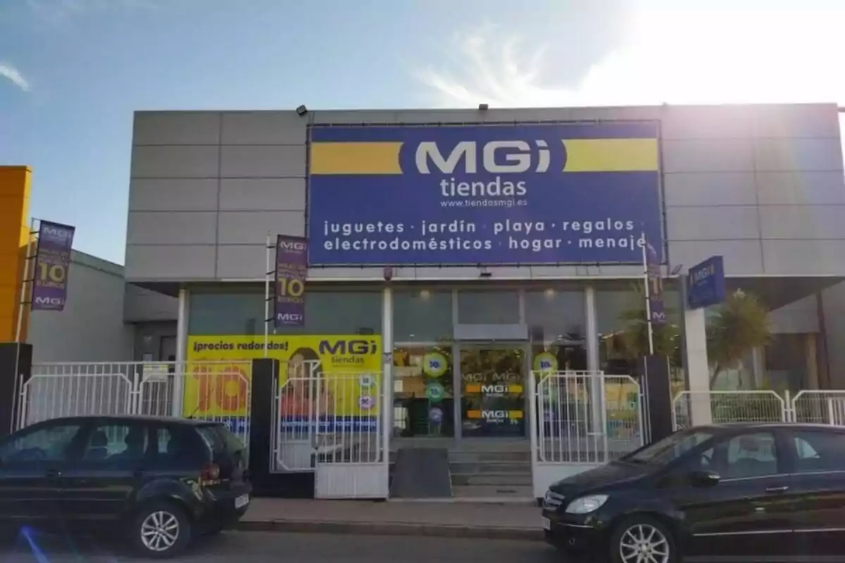 Fachada de una tienda MGI con carteles promocionales y coches estacionados al frente. Fachada de una tienda MGI con carteles promocionales y coches estacionados al frente.