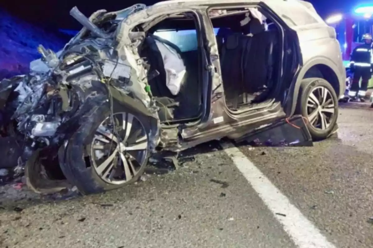 Vehículo SUV gravemente dañado tras un accidente en carretera con presencia de servicios de emergencia al fondo Vehículo SUV gravemente dañado tras un accidente en carretera con presencia de servicios de emergencia al fondo