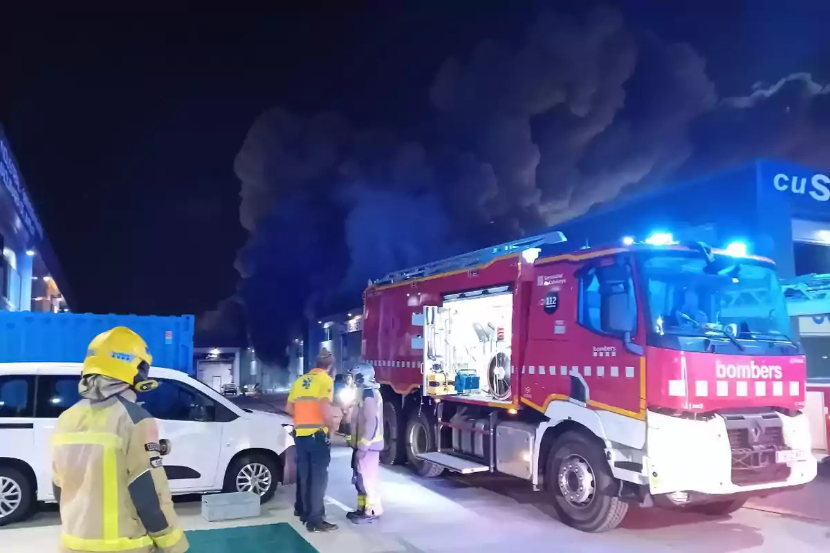 Bomberos y personal de emergencia trabajando en la escena de un incendio nocturno con un camión de bomberos y humo oscuro en el fondo. Bomberos y personal de emergencia trabajando en la escena de un incendio nocturno con un camión de bomberos y humo oscuro en el fondo.