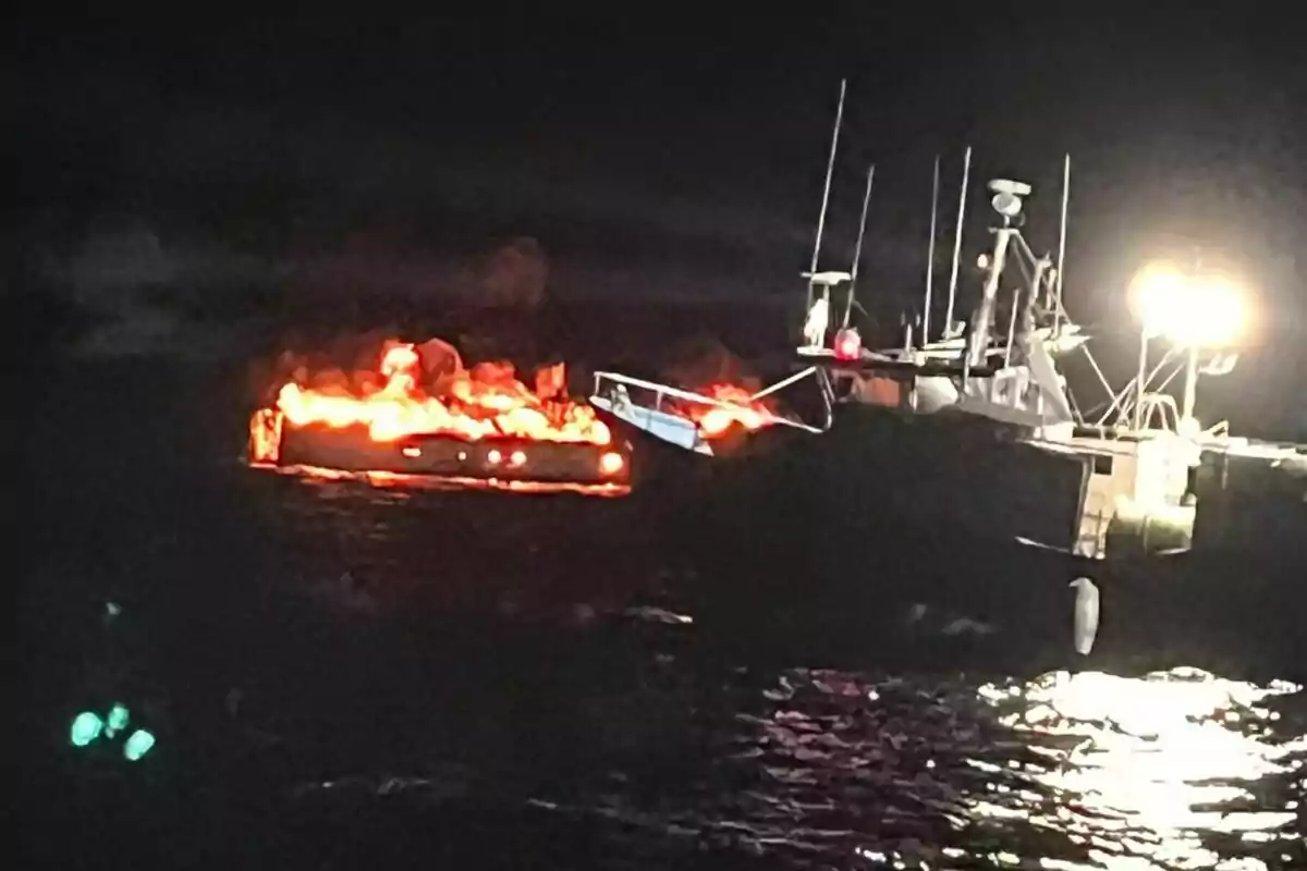 Una embarcación en llamas en el mar durante la noche con otra embarcación iluminada cerca.