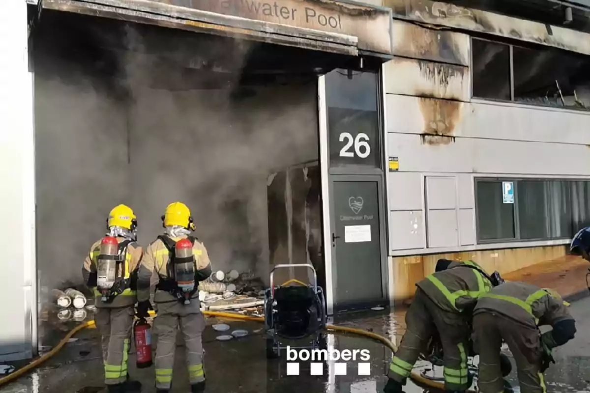 Bomberos trabajando para controlar un incendio en un edificio industrial mientras el humo sale por la puerta. Bomberos trabajando para controlar un incendio en un edificio industrial mientras el humo sale por la puerta.