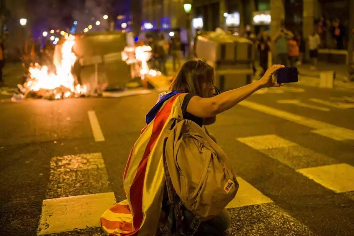 Una manifestante empieza se hace un selfie con un contenedor que se quema durante una manifestación por el referéndum del 1-O en Cataluña,