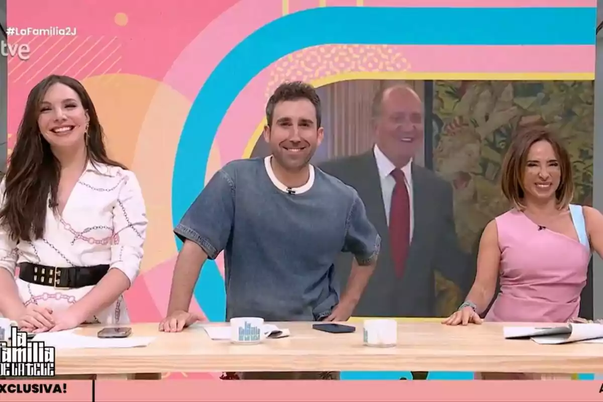Inés Hernand, Aitor Albizua y María Patiño sonríen en un set de televisión de La Familia de la Tele colorido con una pantalla al fondo mostrando a un hombre mayor elegantemente vestido