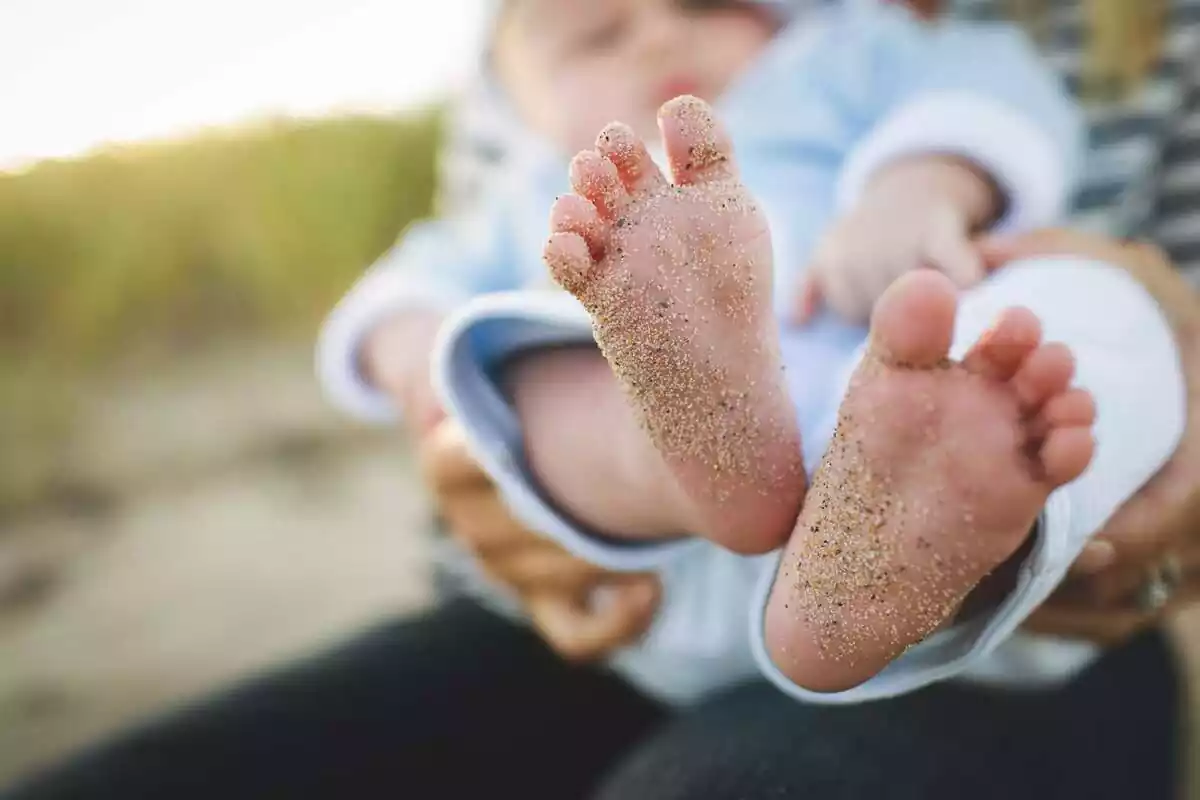Imagen en la que se pueden ver los pies de un infante que está siendo sostenido por otra persona desde atrás