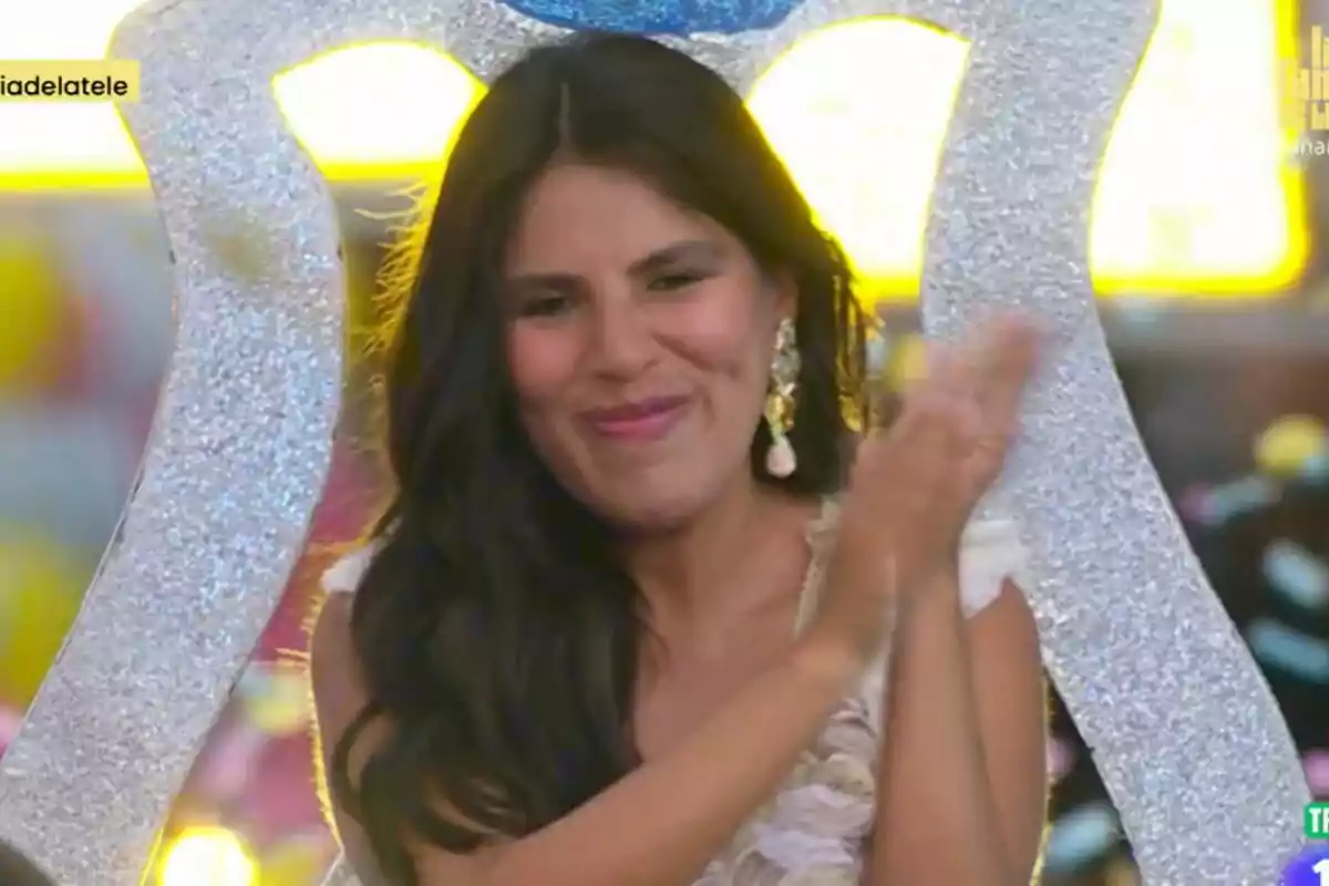 Isa Pantoja con cabello oscuro y largo aplaude mientras sonríe, con un fondo colorido y brillante en el estreno de La Familia de la Tele.