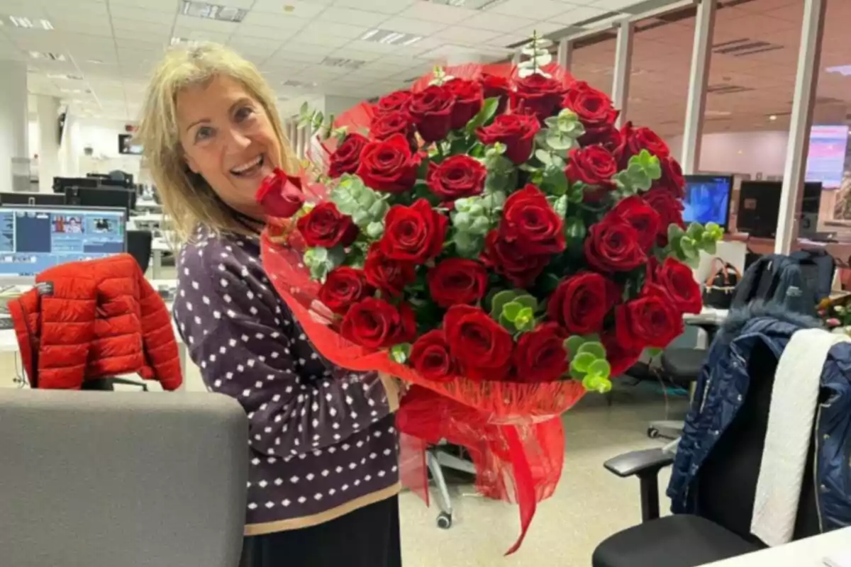 Mujer sonriendo mientras sostiene un gran ramo de rosas rojas en una oficina. Mujer sonriendo mientras sostiene un gran ramo de rosas rojas en una oficina.