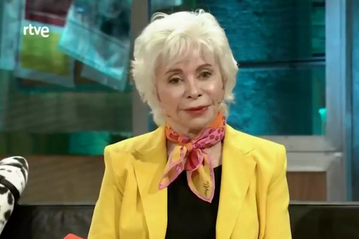 Isabel Allende con cabello blanco y corto lleva un pañuelo colorido y una chaqueta amarilla mientras está sentada en 'La Revuelta'.